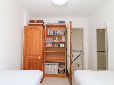 A bedroom with two single beds a wooden wardrobe an open door revealing a hallway and a bookshelf with board games books and baskets at ODYSEA in Weymouth