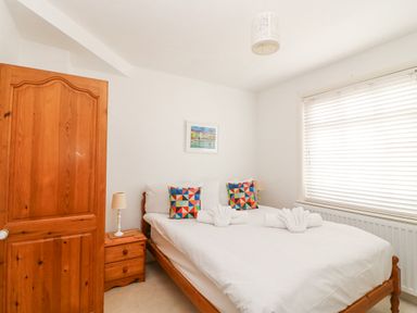 A bedroom with a wooden bed and bedside table with lamps and a window with blinds at ODYSEA Weymouth