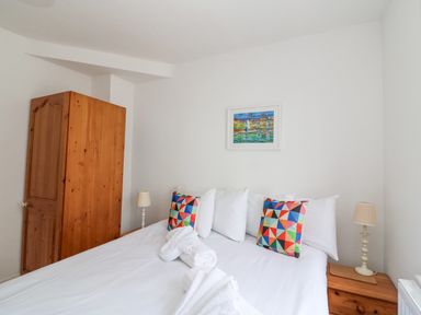 A bedroom with a bed with white linens and colorful pillows a wooden wardrobe and two bedside tables with lamps at ODYSEA Weymouth