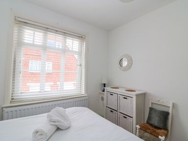 A bedroom with a bed with rolled towels a window with blinds a cabinet with baskets a chair with a cushion and a small mirror on the wall at ODYSEA Weymouth