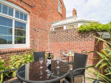 An outdoor patio area with glass table and chairs next to a brick wall at ODYSEA Weymouth