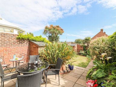A garden patio with black glass table and chairs surrounded by plants and a brick wall at ODYSEA in Weymouth