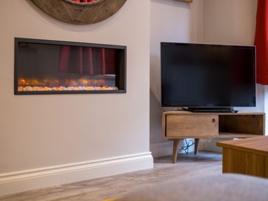 A modern electric fireplace and a flat screen television on a wooden stand in a living room at Howe Keld 1 Ground floor in Keswick