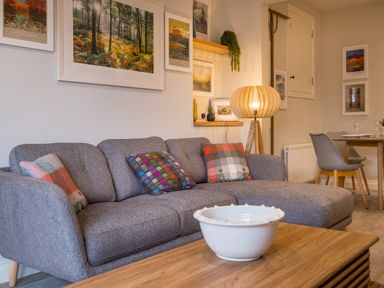 A living room with a grey sofa and colorful cushions a wooden coffee table and lamp at Howe Keld 1 Ground floor in Keswick