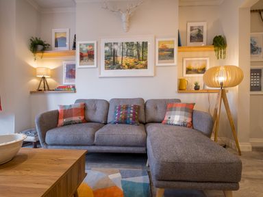 A living room with a gray sectional sofa pillows wooden shelves and lamps at Howe Keld 1 Ground floor in Keswick