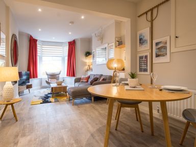 A living room with a gray sofa and red curtains next to a dining table with plates and glasses at Howe Keld 1 Ground floor in Keswick