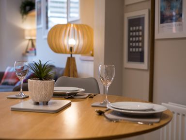 A dining table set with two plates and wine glasses with a potted plant in the center and a lamp in the background at Howe Keld 1 Ground floor Keswick