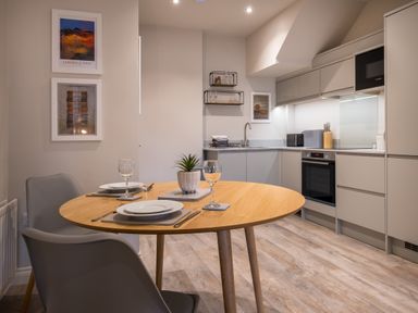 A kitchen with a round wooden dining table set for two and grey cabinets at Howe Keld 1 Ground floor Keswick