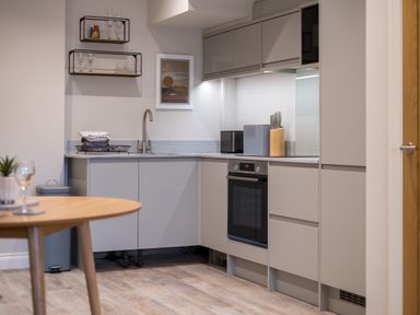 A kitchen with grey cabinets a built in oven a sink and a wooden table with a glass at Howe Keld 1 Ground floor in Keswick