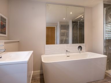 A bathroom with a bathtub sink mirror wooden door and shower at Howe Keld 1 Ground floor in Keswick