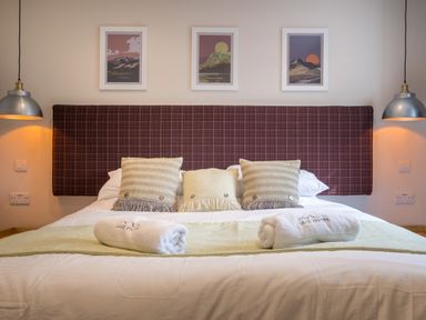 A bed with three pillows and two rolled towels with wall lights and three framed pictures above at Howe Keld 1 Ground floor in Keswick