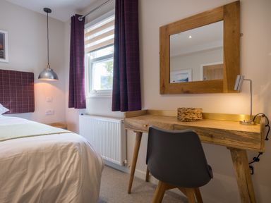 A bedroom with a bed a wooden desk with a lamp and a wicker basket a mirror above the desk and a window with curtains at Howe Keld 1 Ground floor in Keswick