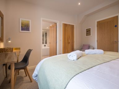 A bedroom with a bed, desk and chair, two wooden doors, and a small armchair at Howe Keld 1 Ground floor in Keswick