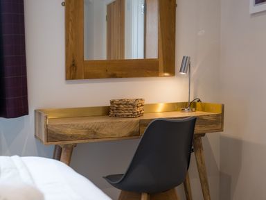 A wooden desk with a mirror above it a small lamp and a woven basket and a black chair in a room at Howe Keld 1 Ground floor in Keswick