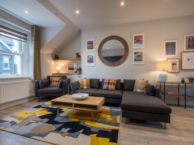 A living room with a dark gray sofa and armchair with plaid cushions and a wooden coffee table on a colorful rug at Howe Keld 4 First floor in Keswick