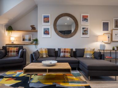 A living room with a sectional sofa and armchair a wooden coffee table and a large round mirror on the wall at Howe Keld 4 First floor in Keswick