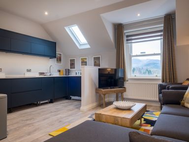 A living room with gray sofa and wooden coffee table next to a kitchen with blue cabinets under skylight window at Howe Keld 4 First floor in Keswick