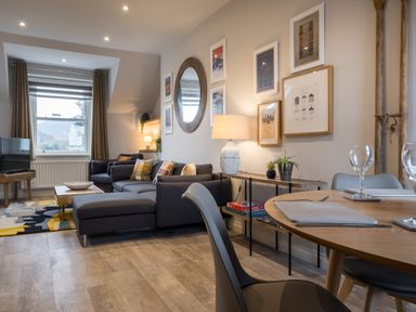 A living room with a gray sectional sofa a coffee table a TV wooden floor and framed pictures on the wall at Howe Keld 4 First floor in Keswick