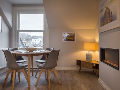 A dining area with a round wooden table four chairs wine glasses and a lamp on a wooden sideboard at Howe Keld 4 First floor in Keswick