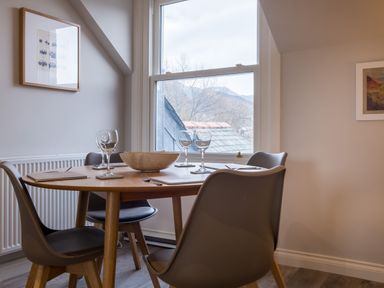 A dining area with a round wooden table four chairs place settings and a window showing rooftops at Howe Keld 4 First floor Keswick