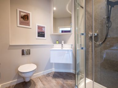 A bathroom with a wall-mounted toilet sink with mirror and shower enclosure at Howe Keld 4 First floor in Keswick