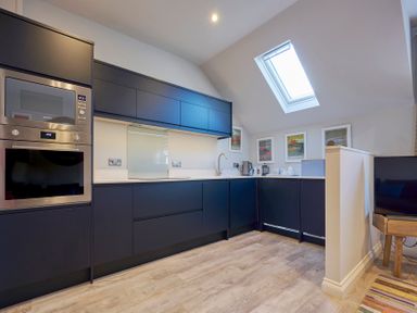 A kitchen with dark cabinets stainless steel appliances a skylight and framed pictures on the wall at Howe Keld 4 First floor in Keswick