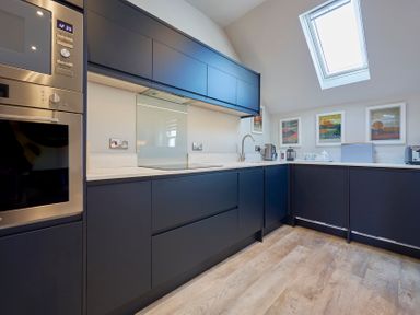 A kitchen with dark cabinets a built-in oven a sink under a skylight and framed pictures on the wall at Howe Keld 4 First floor in Keswick