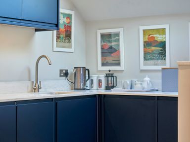 A kitchen corner with blue cabinets metal kettle coffee press canisters and framed posters on the wall at Howe Keld 4 First floor in Keswick