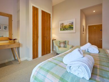 A bedroom with a bed covered with towels a green armchair wooden doors and a wooden dressing table at Howe Keld 4 First floor in Keswick