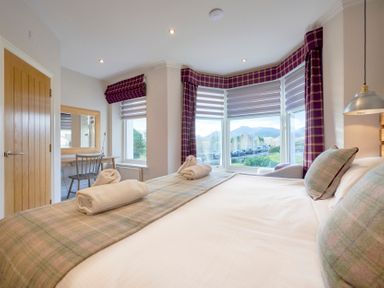 A bedroom with a large bed and rolled towels on it a window with purple plaid curtains and a wooden door at Howe Keld 4 First floor in Keswick