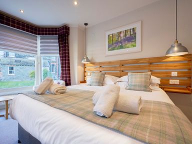 A bedroom with a double bed with rolled towels pillows window with blinds and curtains at Howe Keld 4 First floor Keswick