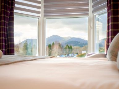 A bed facing large windows with a view of mountains and trees at Howe Keld 4 First floor in Keswick