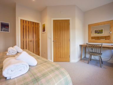 A bedroom with a bed with towels on it wooden doors a wooden desk and a chair at Howe Keld 4 First floor in Keswick