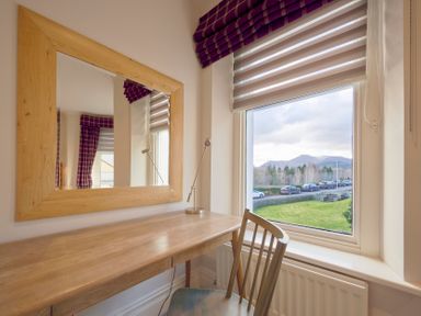 A wooden desk with a chair and a lamp next to a window with striped blinds and a large wooden framed mirror on the wall at Howe Keld 4 First floor in Keswick