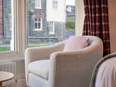 A light grey armchair with a pink cushion beside a window with red and brown plaid curtains at Howe Keld 4 First floor in Keswick