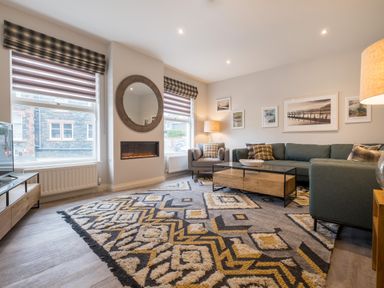 A living room with a patterned rug sofa armchair coffee table and a round mirror at Howe Keld 5 First Floor in Keswick