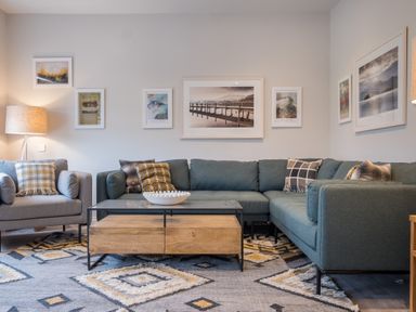 A living room with a gray armchair and sectional sofa a wooden coffee table with a decorative bowl and framed pictures on the walls at Howe Keld 5 First Floor Keswick