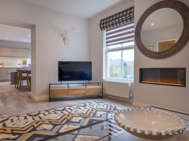A living room with a television on a wooden stand a patterned rug and a round mirror above a fireplace at Howe Keld 5 First Floor Keswick