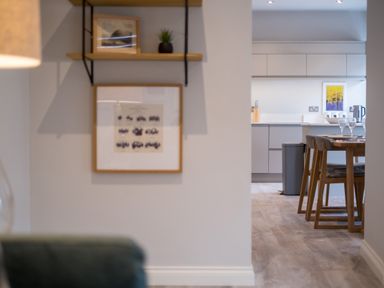 A dining area with wooden chairs and a table set with glasses next to a modern kitchen with gray cabinets and a trash bin at Howe Keld 5 First Floor Keswick