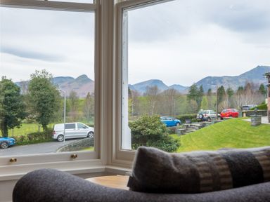 A view through a large window showing parked cars trees and mountains with a sofa in the foreground at Howe Keld 5 First Floor in Keswick