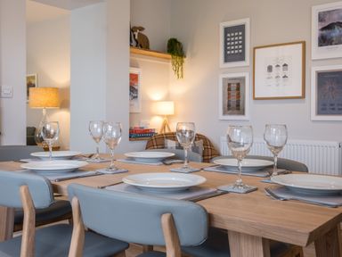 A dining table set with plates and wine glasses in a dining room with framed pictures on the wall at Howe Keld 5 First Floor in Keswick