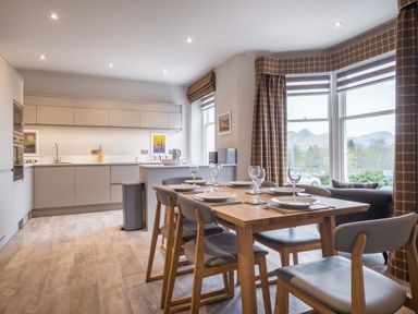 A kitchen and dining area with a wooden table set for six near large windows with checkered curtains at Howe Keld 5 First Floor in Keswick