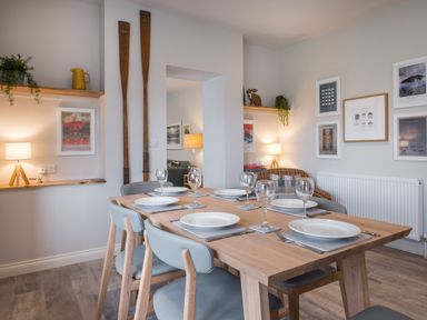 A dining room with a wooden table set for six with chairs and wall art at Howe Keld 5 First Floor in Keswick