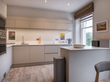 A kitchen with gray cabinets a countertop a sink a microwave kettle and framed pictures by a window at Howe Keld 5 First Floor in Keswick