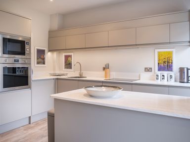A kitchen with gray cabinets a built in oven and microwave a sink a stovetop a bowl on the island and framed pictures on the wall at Howe Keld 5 First Floor in Keswick