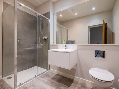 A bathroom with a glass shower enclosure a wall-mounted sink with a mirror and a wall-mounted toilet at Howe Keld 5 First Floor in Keswick