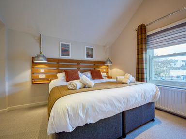 A bedroom with a double bed two rolled towels hanging pendant lights and a window showing buildings outside at Howe Keld 5 First Floor in Keswick