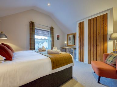 A bedroom with a bed table with mirror wooden closet and an armchair at Howe Keld 5 First Floor in Keswick