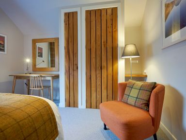 A bedroom with an orange chair and plaid cushion a wooden desk with chair and a mirror and wooden closet doors at Howe Keld 5 First Floor in Keswick