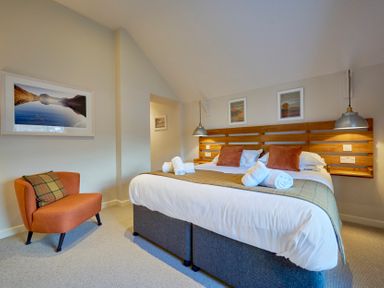 A bedroom with a double bed with pillows and rolled towels an orange chair and framed pictures on the walls at Howe Keld 5 First Floor in Keswick